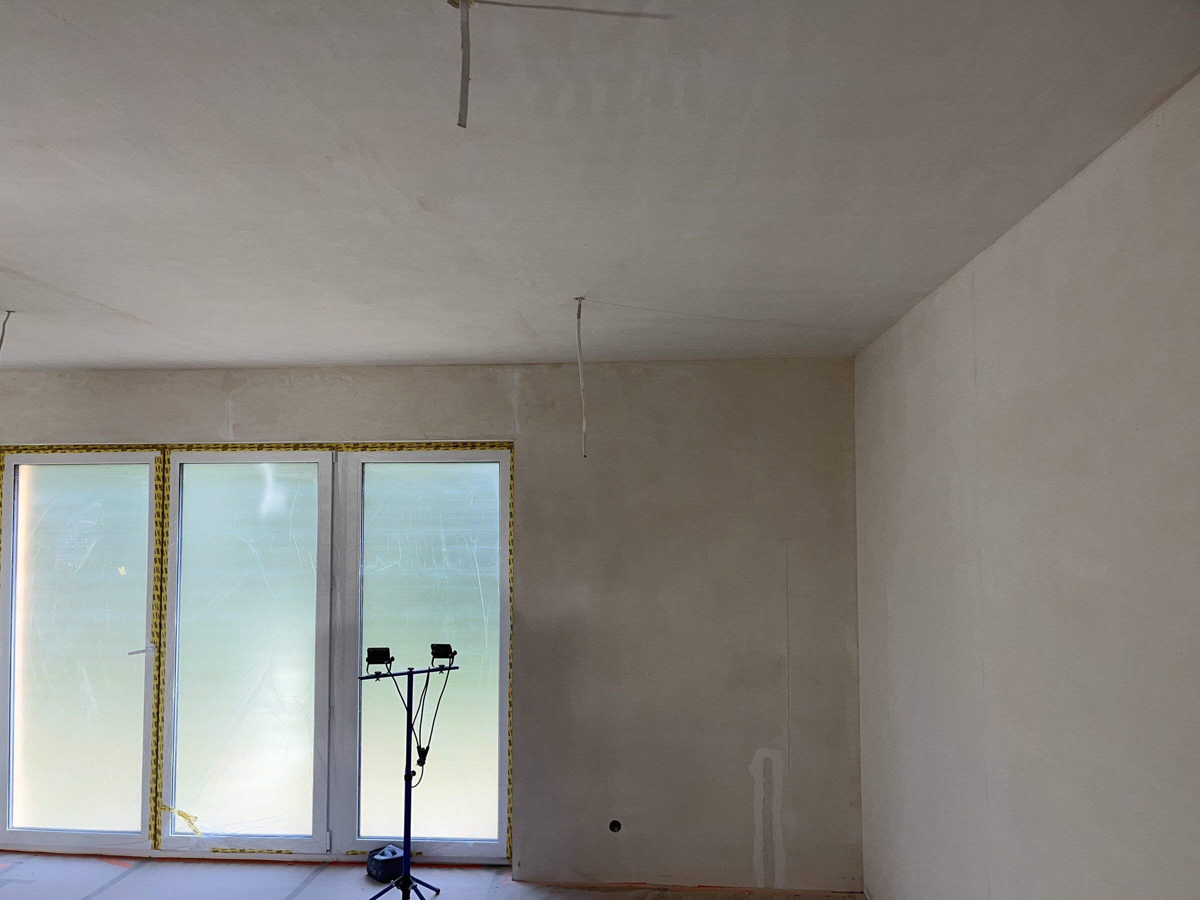 Salon po nałożeniu gładzi, okna zabezpieczone folią, oświetlenie robocze